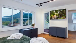 Un dormitorio moderno con un gran ventanal, una cama, un aparador y un televisor.