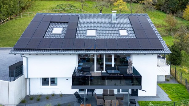 Una casa moderna de dos pisos con techo plano, ventanas amplias y un balcón con mobiliario exterior.
