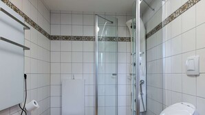 Un baño pequeño con inodoro, cabina de ducha de vidrio y lavamanos.