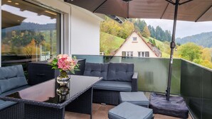 Un balcon extérieur aménagé avec des meubles en osier, une table en verre et un grand parasol.