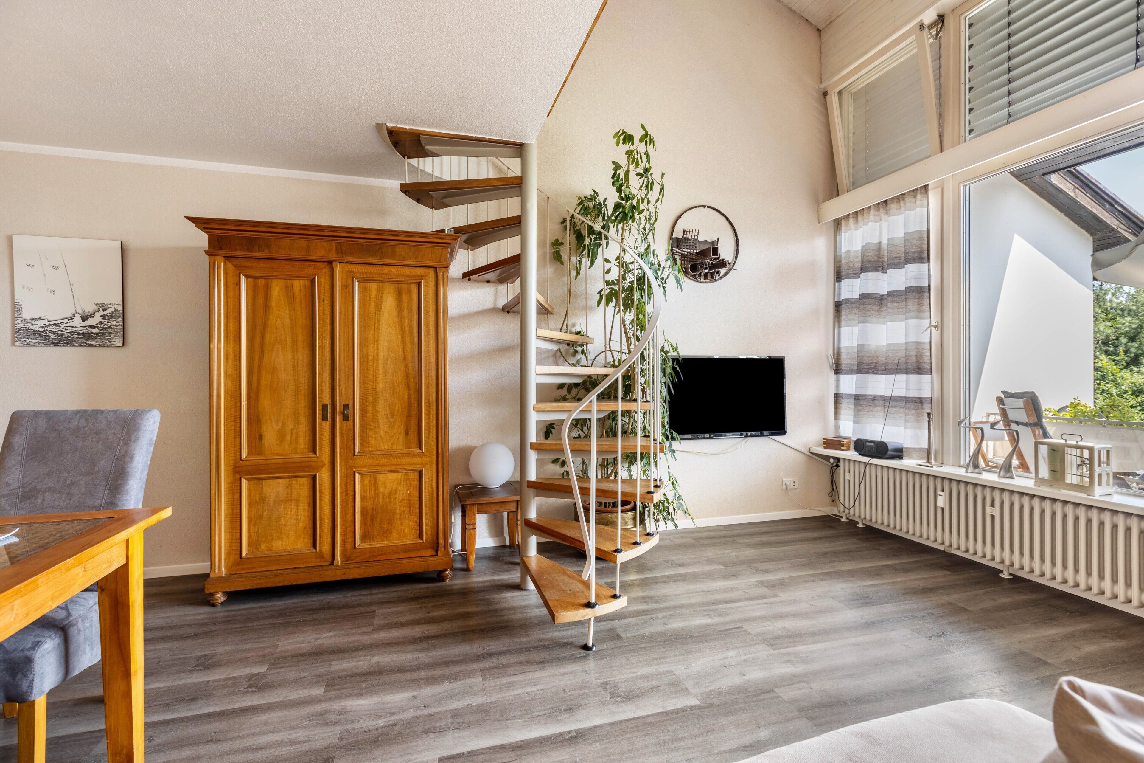 Un salon moderne avec un meuble en bois, un escalier en colimaçon, une grande fenêtre et un téléviseur.