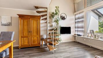 Un salon moderne avec un meuble en bois, un escalier en colimaçon, une grande fenêtre et un téléviseur.