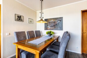 Un coin repas comprenant une table à plateau en verre, des chaises à revêtement gris, un luminaire suspendu et des œuvres d’art accrochées aux murs.