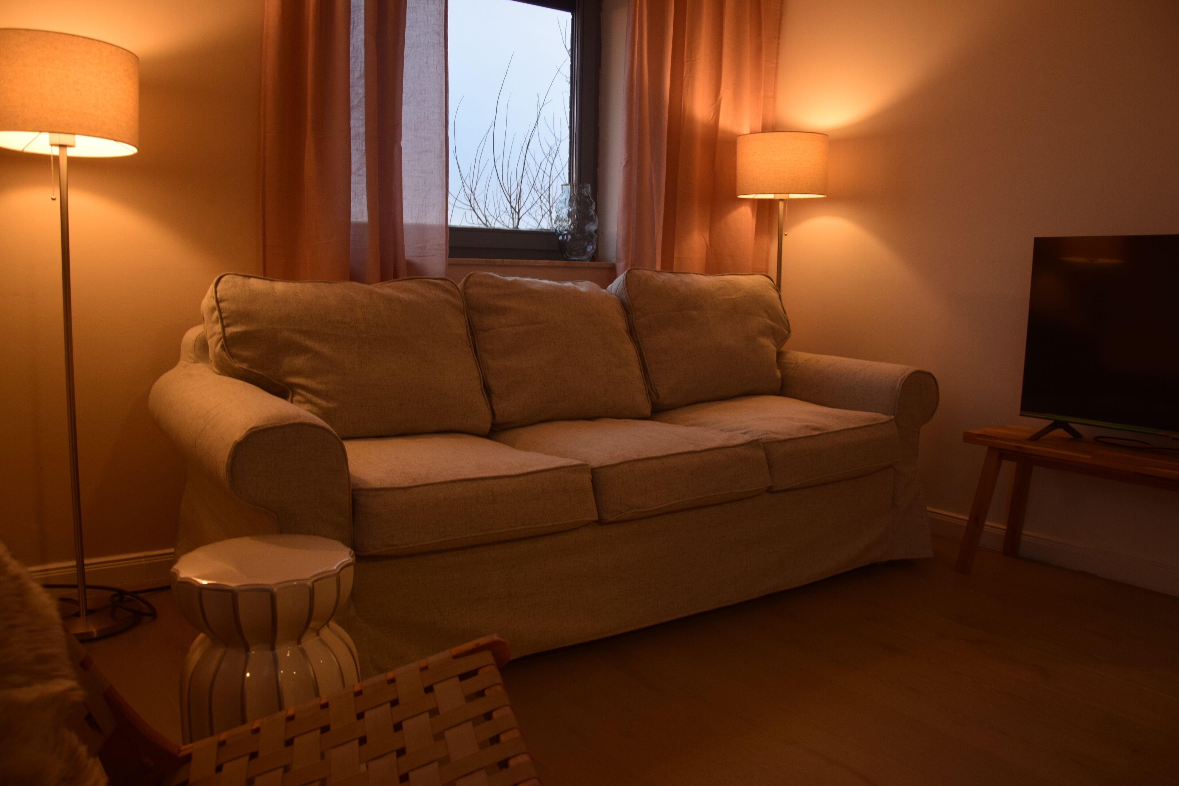 Ett vardagsrum med en soffa, två golvlampor, ett litet bord och en tv.