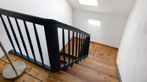 Un escalier en bois avec une rampe noire, des murs blancs et une lucarne.