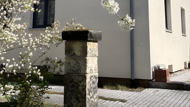 Un bâtiment aux murs blancs, orné d’une colonne de pierre et de fleurs blanches en pleine floraison.