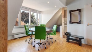 Une pièce avec un plafond en pente, une table ronde, des chaises vertes, un banc et un miroir au mur.
