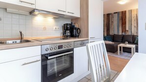 A modern kitchen with white cabinetry, a built-in oven, a coffee maker, and a dining area with a white chair and table. - Apartment 'Malia', Shared Terrace and Wi-Fi (Büsum)