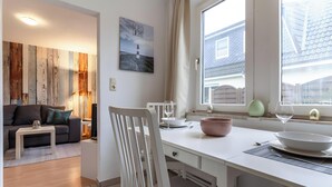 A modern living room with a sofa, coffee table, and a dining area with a table, chairs, and a window with curtains. - Apartment 'Malia', Shared Terrace and Wi-Fi (Büsum)
