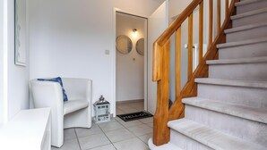 A staircase with wooden handrails, a white couch with a blue pillow, a small table, and a door leading to another room. - Apartment 'Malia', Shared Terrace and Wi-Fi (Büsum)