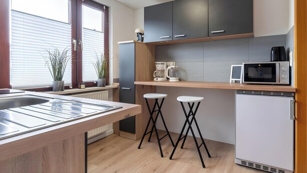 Una cocina moderna con horno empotrado, microondas y cafetera. Hay dos taburetes y un refrigerador pequeño.