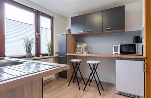 Una cocina moderna con horno empotrado, microondas y cafetera. Hay dos taburetes y un refrigerador pequeño.
