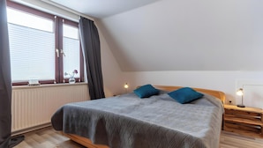 Un dormitorio con cama, ventana con cortinas, mesita de noche con lámpara y radiador.