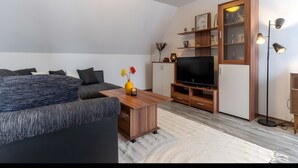 Una sala moderna con sofá, mesa de centro, televisor, mueble de madera y lámpara de pie.