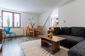 Una sala de estar con un sofá, una mesa de centro con un florero, una mesa de comedor con sillas y una ventana con persianas.