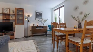 Una sala de estar moderna con televisor de pantalla plana, muebles de madera, una mesa de comedor y un ventanal con persianas.