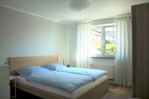 Una cama individual con cabecera de madera, una mesita de noche y una ventana con cortinas.