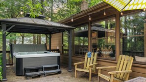 Een houten terras met een jacuzzi, een overdekte zithoek en uitzicht op het bos.