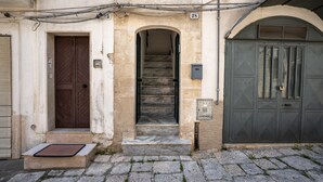A building with a stone facade, a wooden door, a staircase leading to an upper floor, and a metal gate.