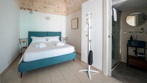 A bedroom with a bed, a vanity with a mirror, and a shower.