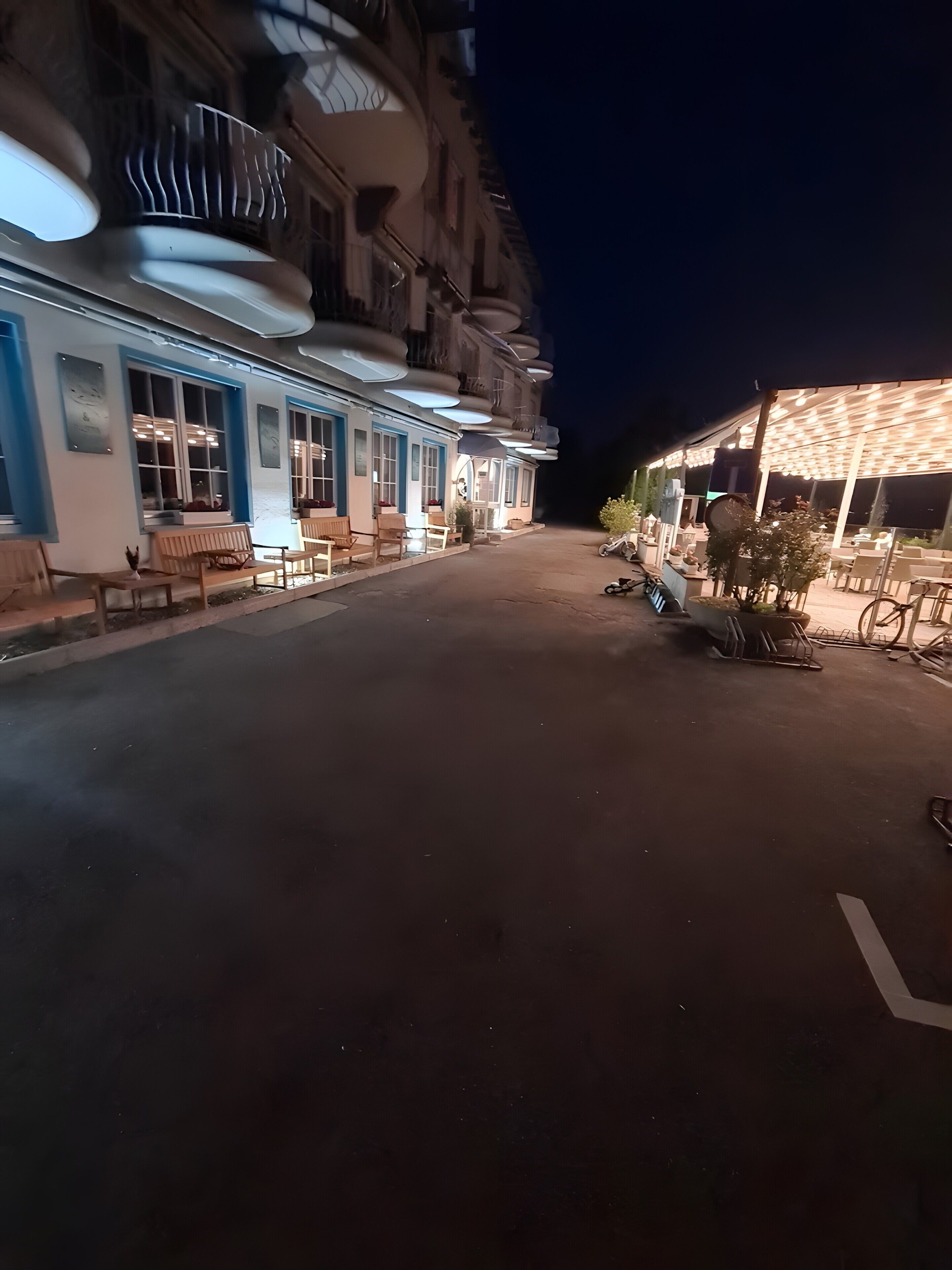 Une vue de rue nocturne, avec un bâtiment doté de grandes fenêtres et d’une terrasse.