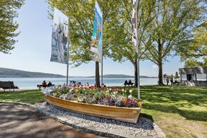 Een park aan het water met een bloemenbak in de vorm van een boot, bankjes en vlaggen.