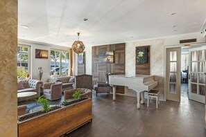 Een ruime woonkamer met een vleugelpiano, comfortabele zitplaatsen en een groot raam.
