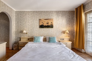 A hotel room with a large bed, two bedside tables with lamps, a wall-mounted picture, and a window with curtains.