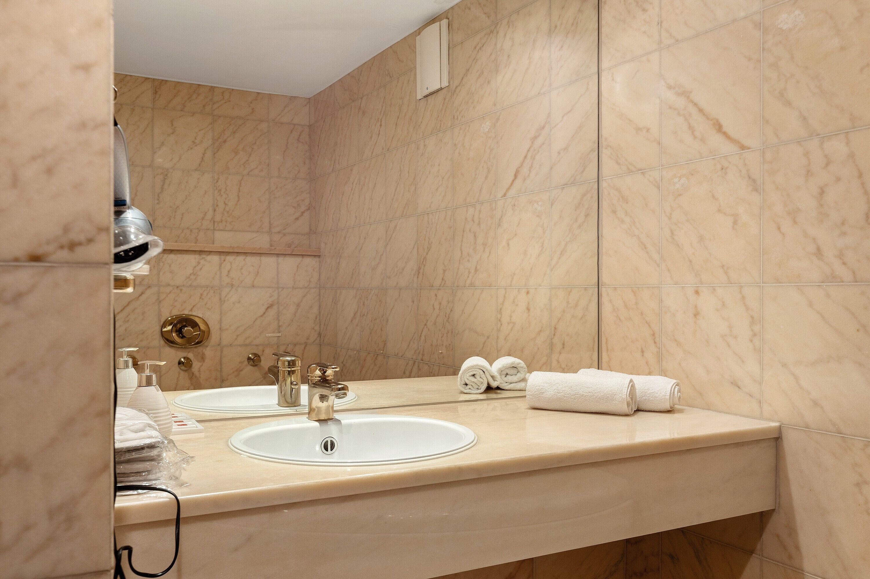 Un baño con lavamanos de mármol, un espejo y dos toallas.