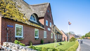 Een gebouw van baksteen met een rieten dak, een stenen muur en een wapperende vlag aan een mast.