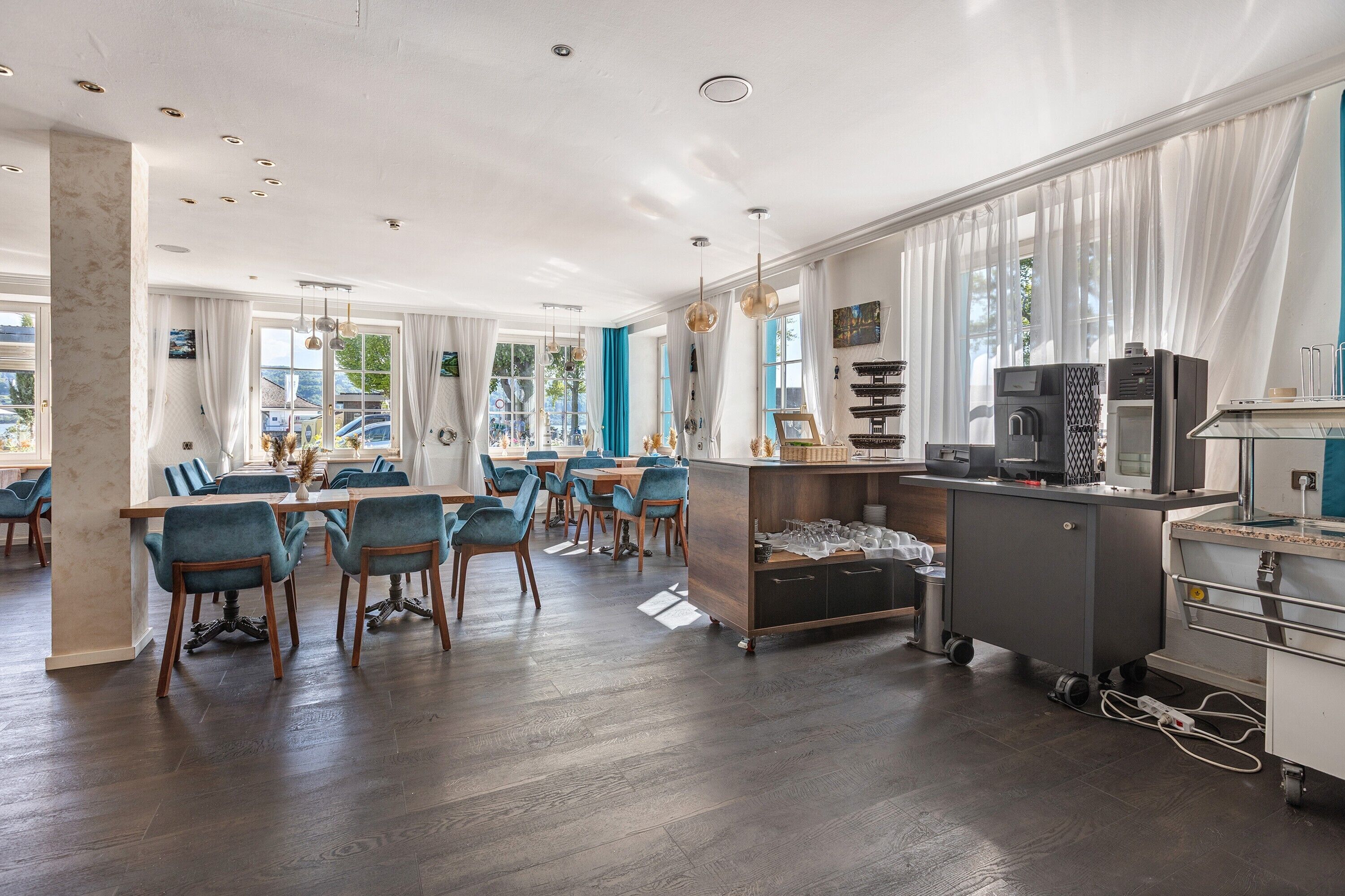 A modern dining area with a long table, blue chairs, and a kitchen area with appliances.