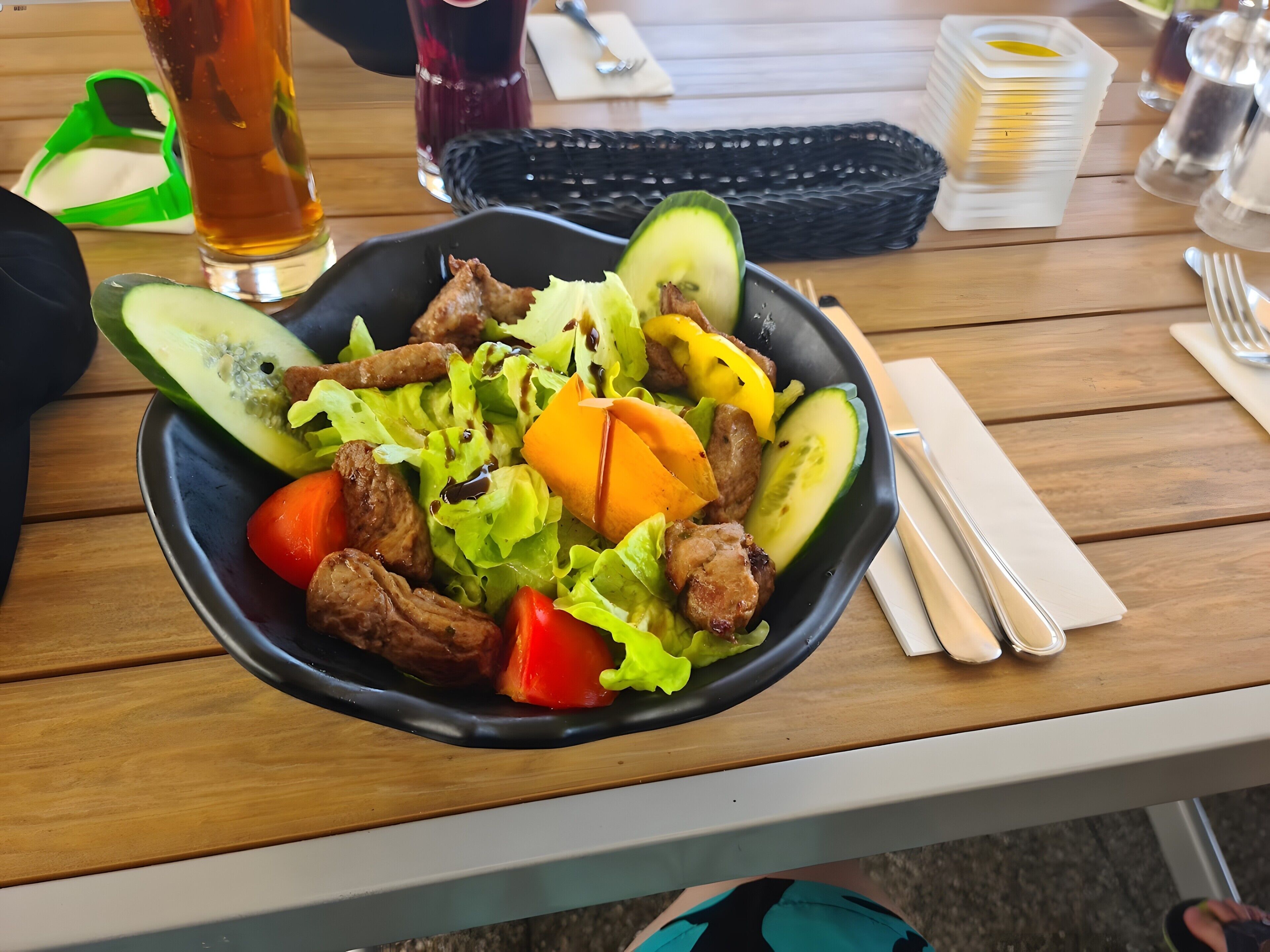 Een saladeschaal met verschillende groenten en vlees op een houten tafel.