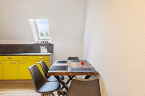 Zona pranzo con tavolo in legno, quattro sedie, una finestra e mobili contenitori gialli.