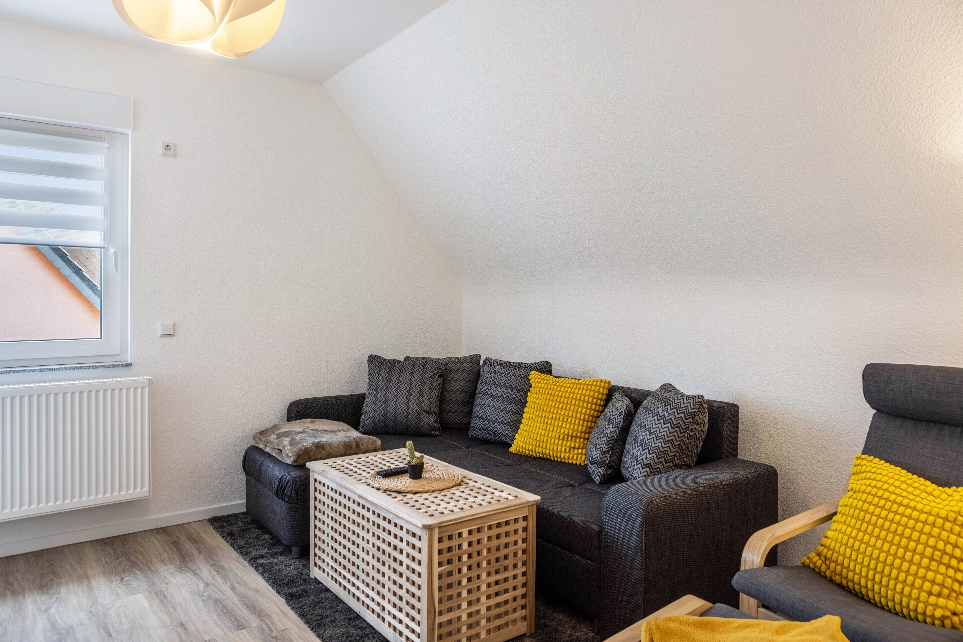 Een moderne woonkamer met een bank, fauteuils, een salontafel en een raam met luxaflex.