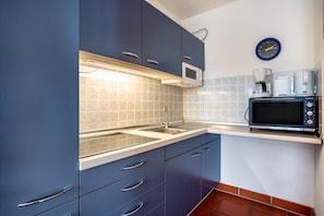 Une cuisine avec des meubles bleus, un four à micro-ondes, une machine à café et une horloge au mur.