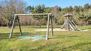 Un parque infantil con columpios y tobogán, rodeado de árboles.