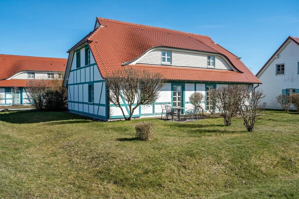 A traditional half-timbered house with a red-tiled roof, surrounded by a well-maintained lawn and a few small trees.