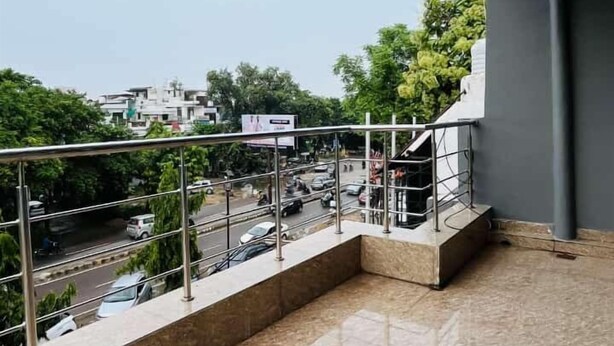 Un balcon doté d’un sol carrelé, d’une rambarde en métal et offrant une vue sur une rue animée, avec des voitures et des immeubles.
