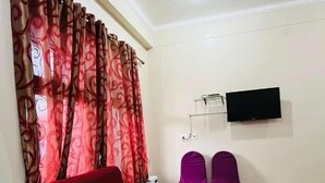 Une pièce avec un canapé rouge, une table en bois, deux fauteuils violets et un téléviseur à écran plat fixé au mur.