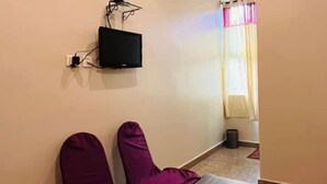 Un couloir avec une table en bois et deux chaises violettes, un téléviseur fixé au mur et une fenêtre avec des rideaux.