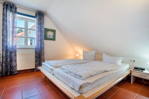 A single bed in a room with a sloped ceiling, a window with curtains, a radiator, and a bedside table with a lamp. - Apartment 'B 53' with Wi-Fi (Dranske)