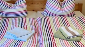 Kaksi sänkyä, joissa on raidalliset vuodevaatteet, tyynyt ja siististi taitetut pyyhkeet.