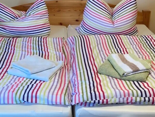 Deux lits avec des draps à rayures, des oreillers et des serviettes pliées.