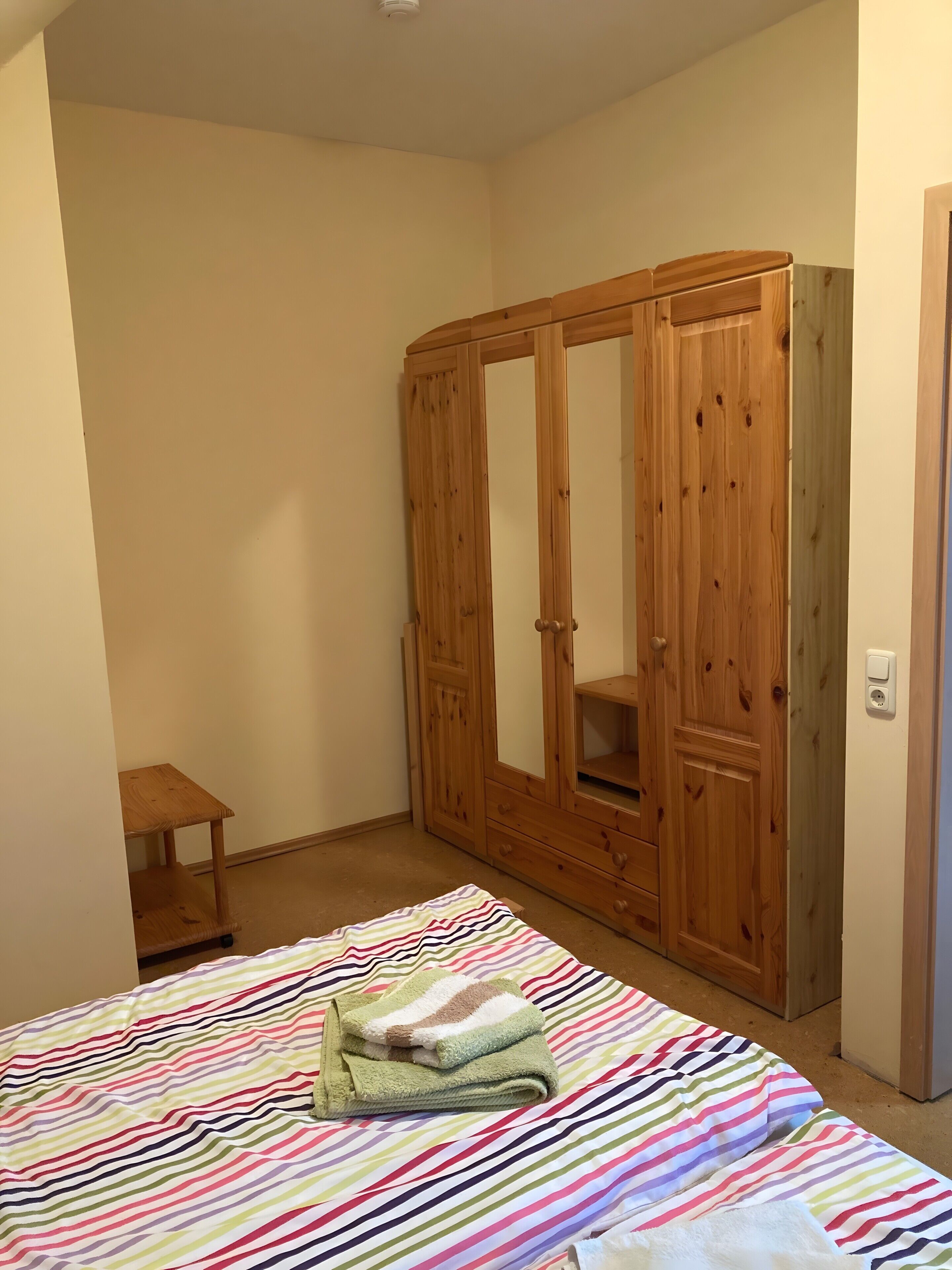 Een slaapkamer met een bed, een houten garderobe en een klein houten tafeltje.