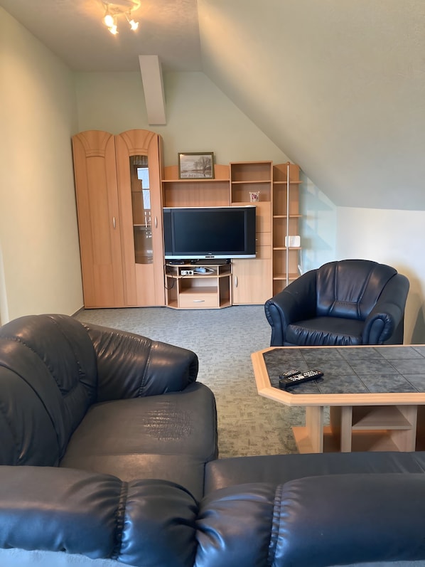 Una sala de estar con televisión, dos sofás de cuero, una mesa de centro y estanterías de madera.