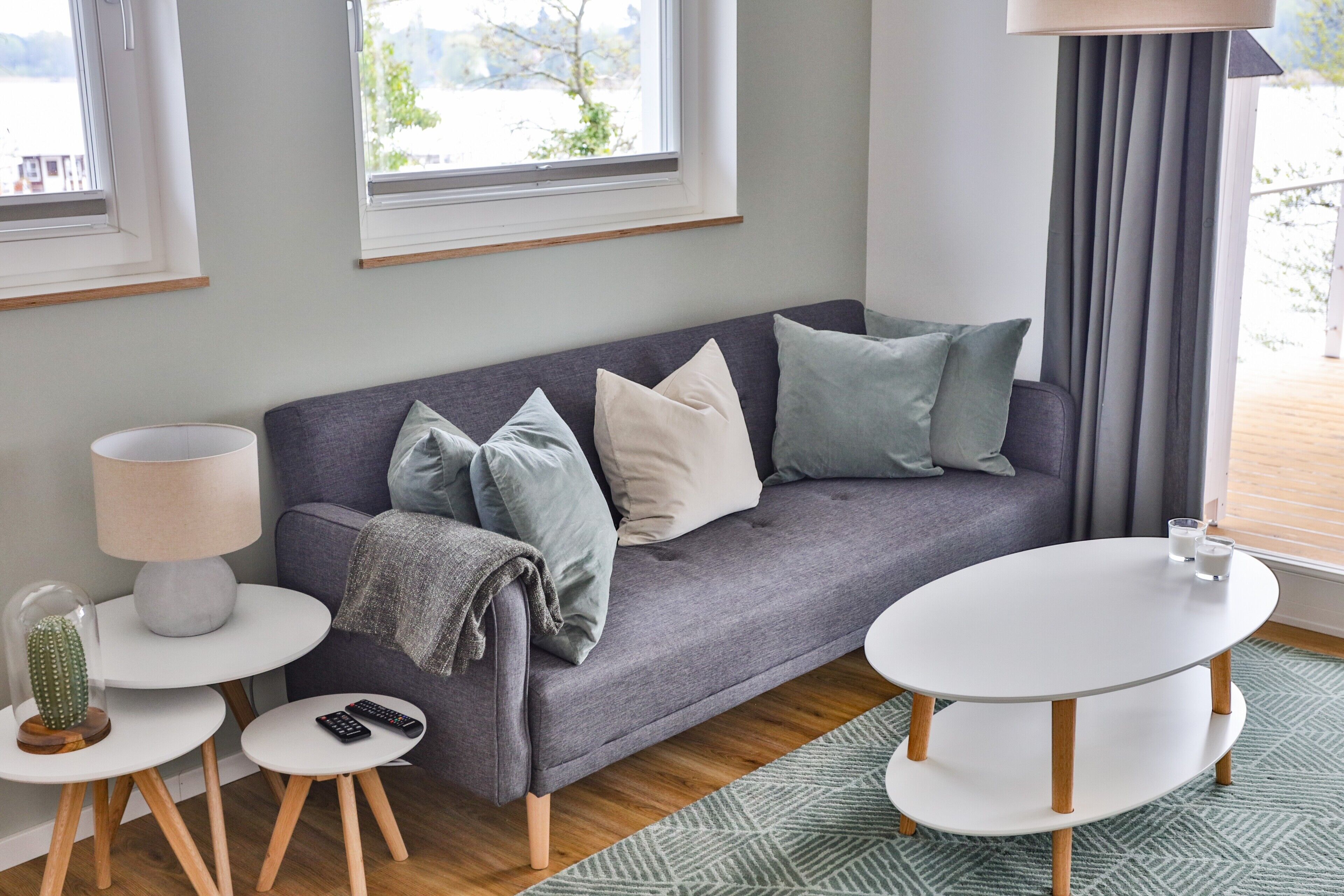 A modern living room with a grey sofa, a white round table, a lamp, and a cactus on a side table.