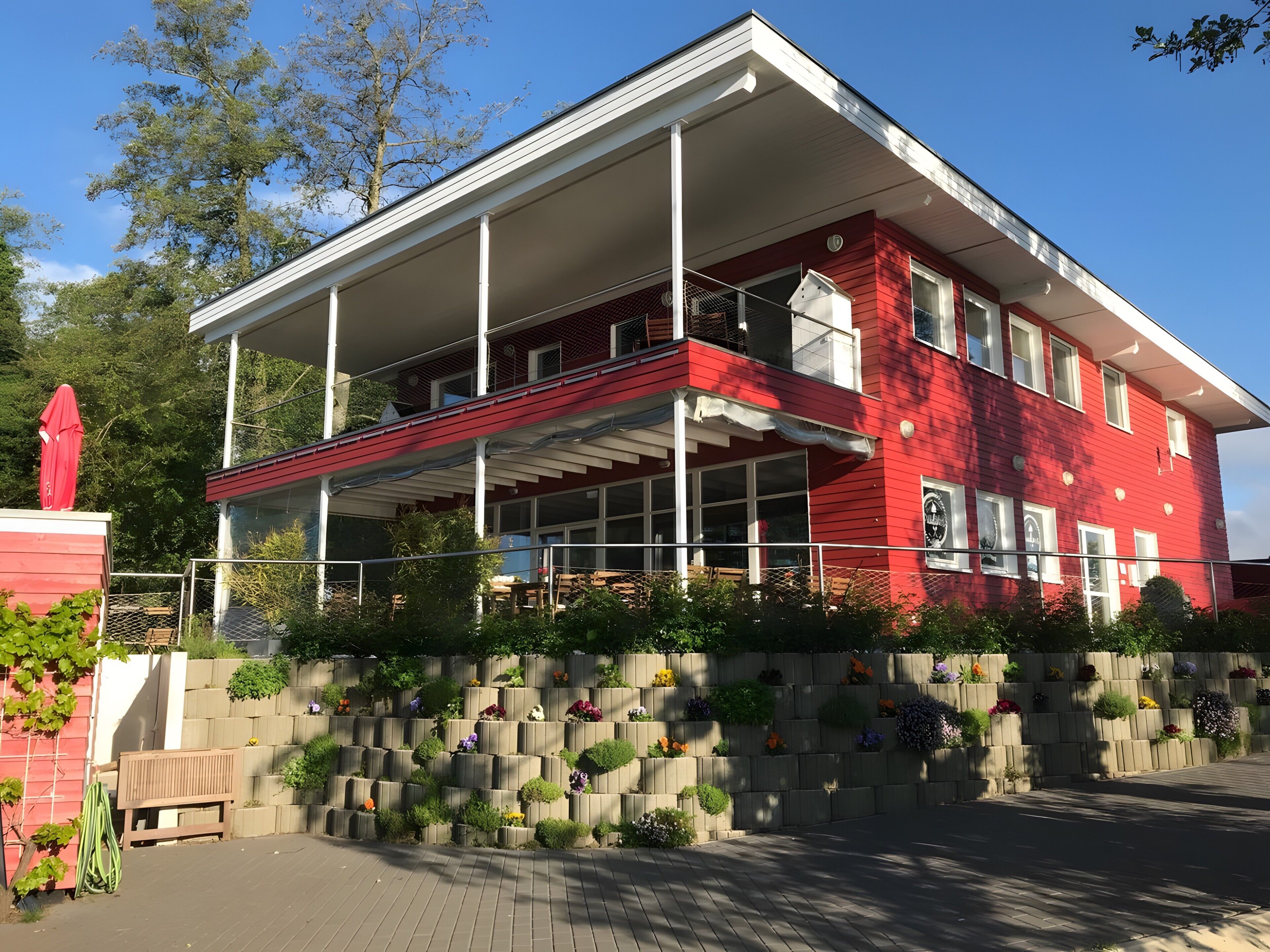 A red building with a balcony, a covered porch, and a flower wall.