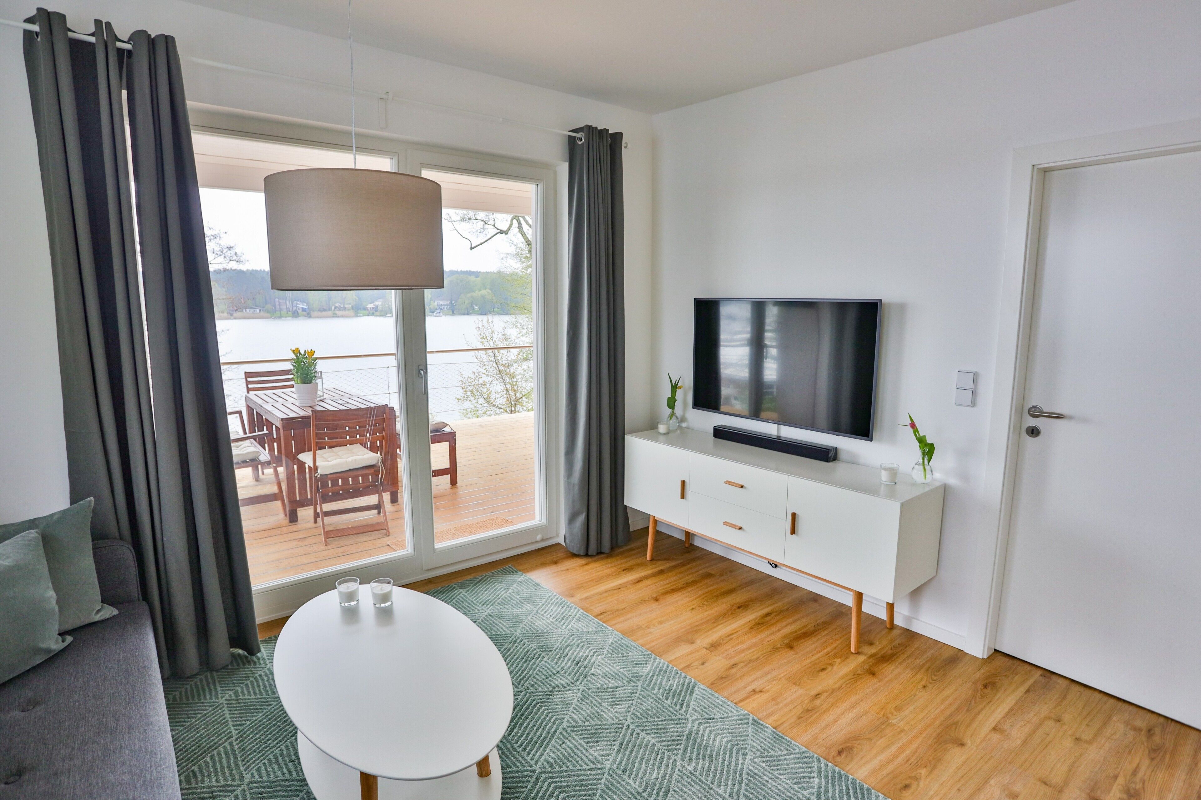 A modern living room with a sofa, a dining table, a TV, and a sliding glass door leading to an outdoor area.