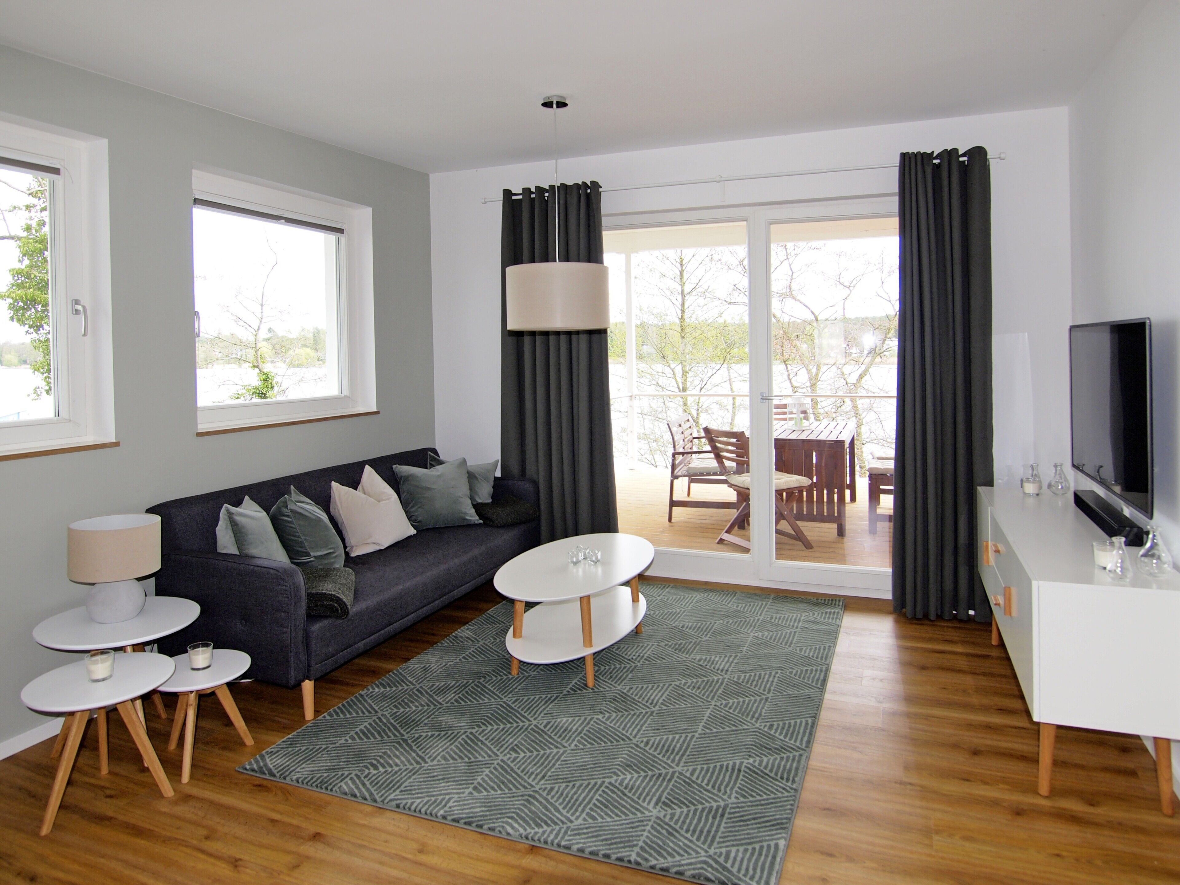 A modern living room with a sofa, coffee table, and TV stand, large windows, and a sliding glass door to an outdoor area.