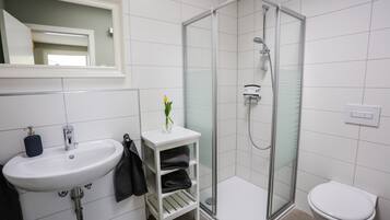 Une salle de bain avec un lavabo blanc, une douche à parois de verre et des toilettes blanches.